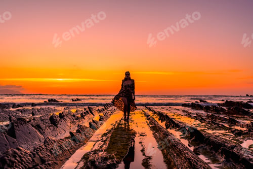 Preview: Young girl with open arms in the water by the rocks