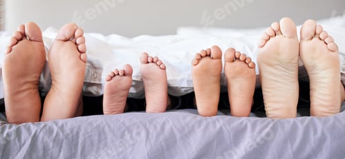 Preview: Feet of family lying in bed. Closeup of feet of parents and children in bed. Family relaxing in bed