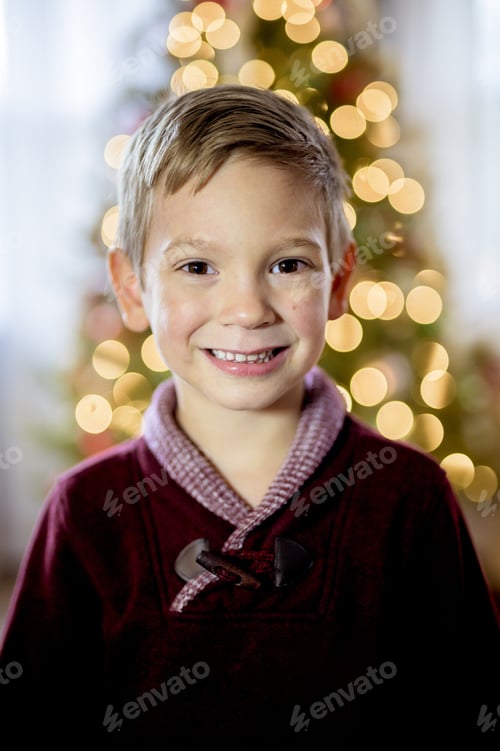 Preview: Vertical shot of a child smiling at the camera with a blurred Christmas tree in the background