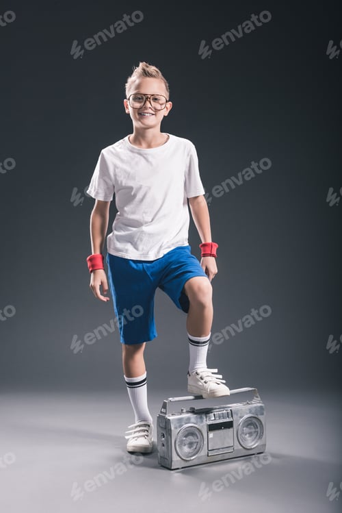Preview: smiling preteen boy in eyeglasses with boombox posing on grey backdrop