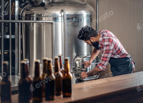 Preview: Indianr male manufacturer presenting craft beer in the microbrewery.