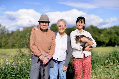 Preview: Smiling woman holding grey cat standing outdoors, with an elderly man and woman, smiling at the