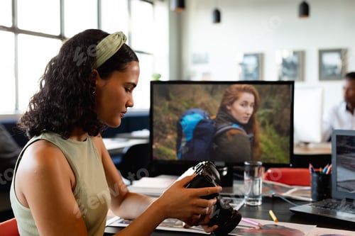 Preview: Biracial young businesswoman examining camera at desk in office