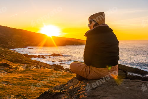 Preview: A relaxed young woman watching the sunset in the cove of stones