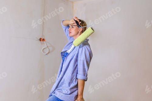 Preview: Repair work of home. Woman paints wall with roller in new apartment.