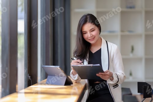 Preview: Asian businesswoman sitting happily working on a laptop Take notes and smile happily on assignment.