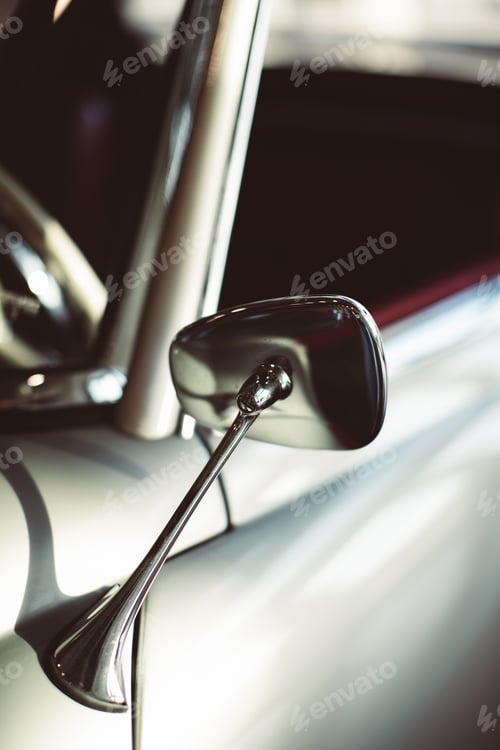 Preview: Vertical closeup shot of the side mirror of a retro car with a blurred background