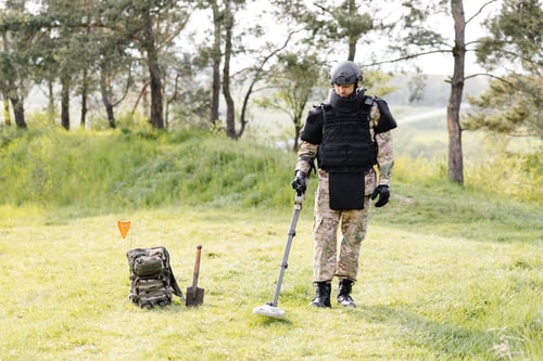 Preview: A man in a military uniform and bulletproof vest works in the forest with a metal detector.