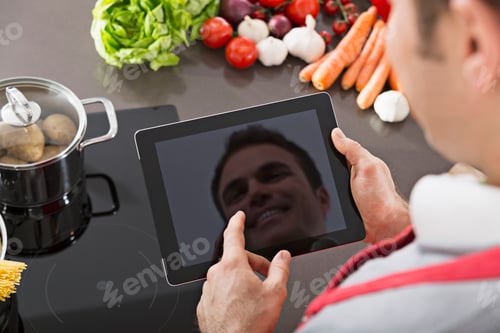 Preview: Display of digital tablet reflecting mirror image of smiling man in a kitchen