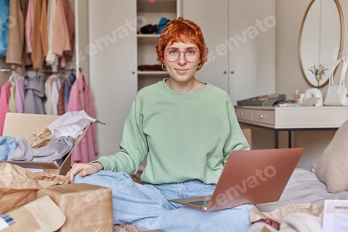 Preview: Serious redhead woman wears casual clothes spectacles makes shopping online via laptop computer