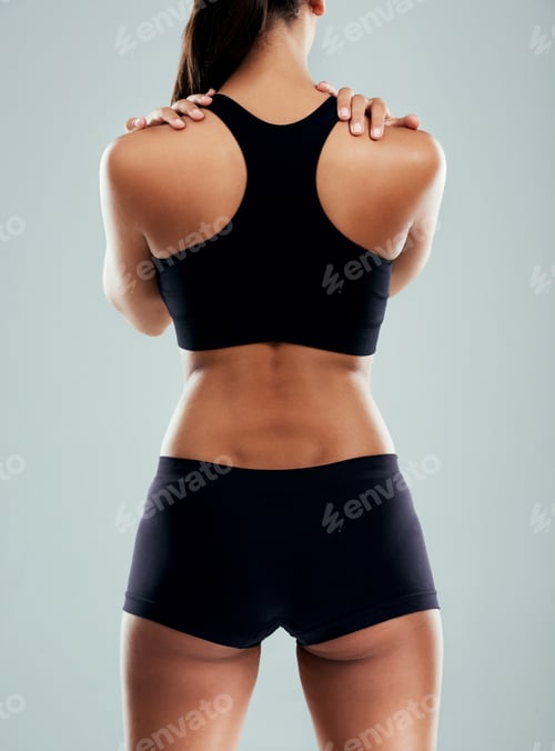 Preview: Rearview shot of a sporty young woman suffering from back pain against a grey background