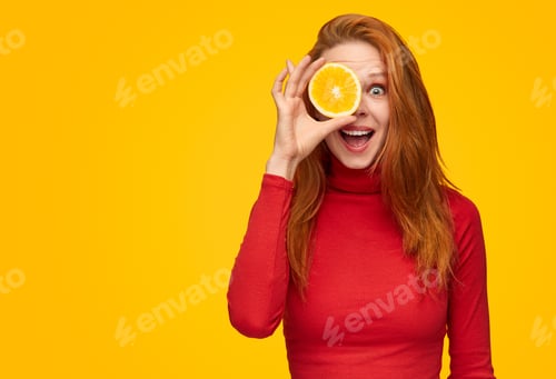 Preview: Expressive girl covering eye with orange slice
