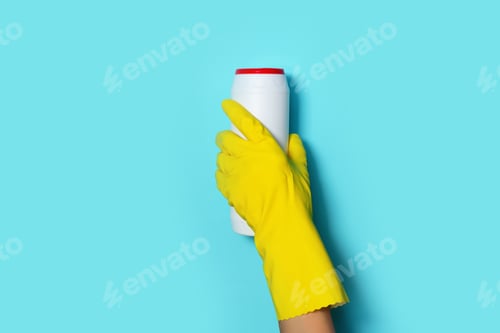Preview: Hand in glove holding white plastic bottle of cleaning product, household chemicals. Copy space