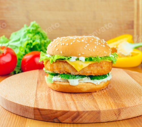 Preview: Crispy chicken sandwich topped with cheese and fresh vegetables on a wooden board