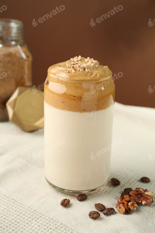Preview: Delicious dalgona coffee in glass, beans, walnuts and granules on table, closeup