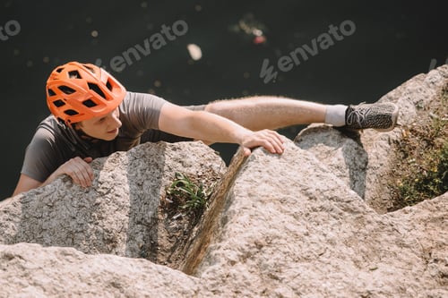 Preview: high angle view of focused male hiker in protective helmet climbing on rocks