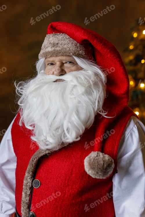 Preview: Close up Santa portrait with white beard and red hat by glowing Christmas lights