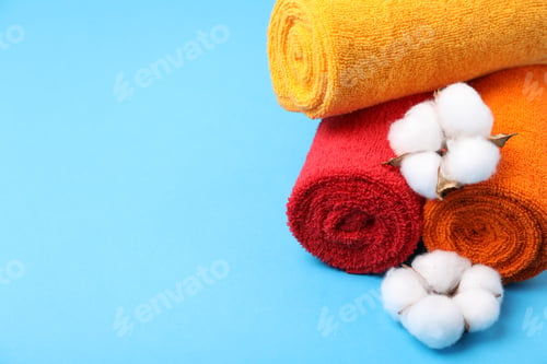 Preview: Clean terry towels and cotton flowers on light blue background, closeup. Space for text