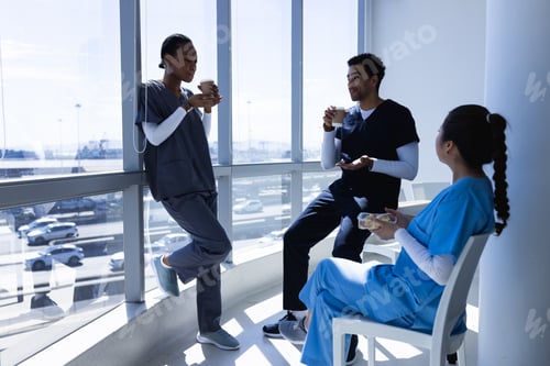 Preview: Diverse male and female doctors talking, drinking coffee and eating lunch in sunny hospital