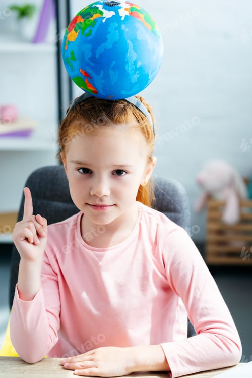 Preview: beautiful schoolgirl with globe on head looking at camera and pointing up with finger