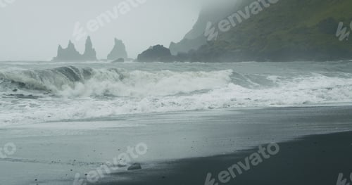 Preview: The black sand beach of Reynisfjara with waves hitting the shore on foggy rainy stormy day Vik