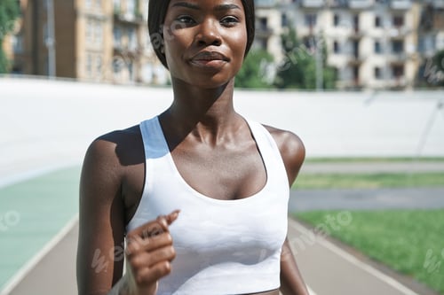 Preview: Close-up of beautiful young African woman in sports clothing running on track outdoors