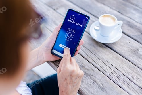 Preview: Senior woman using smart home iot app control on mobile phone to program a washing machine