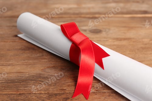 Preview: Rolled student's diploma with red ribbon on wooden table, closeup
