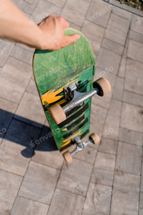 Preview: Close-up of skateboard that a skateboarder holds in his hand in a public park