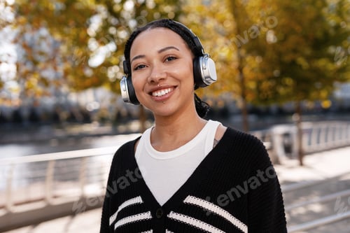 Preview: Young smiling African American woman enjoying music outdoors in autumn