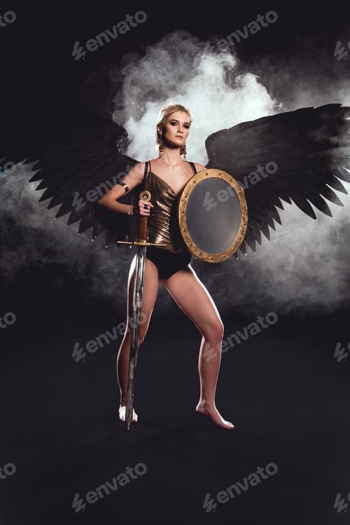 Preview: beautiful woman in warrior costume and angel wings posing with shield and sword on black background