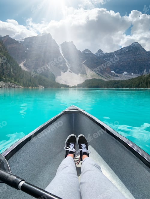 Preview: Young girl stretched out legs in a canoe on Moraine Lake turquoise blue water with view of mountains
