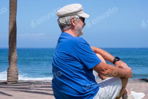 Preview: Senior man sitting alone facing the ocean enjoying a peaceful moment by the seaside