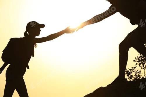 Preview: Silhouettes of man and woman helping each other to climb on hill against sunset