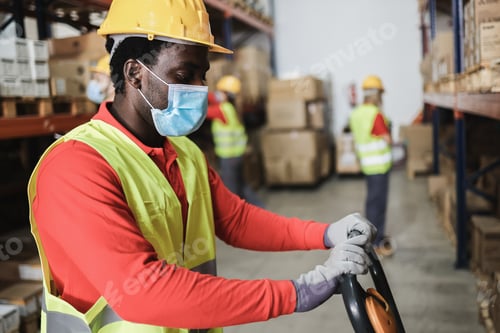 Preview: African warehouse worker loading delivery boxes while wearing safety mask - Focus on man face