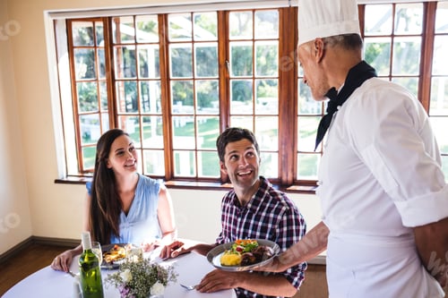 Preview: Chef serving food to young couple sitting in a restaurant