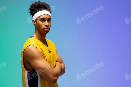 Preview: Male basketball player crossing arms in studio, wearing yellow jersey and headband, copy space