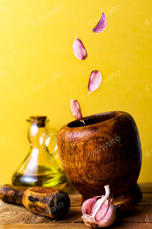 Visualização: Conceito de dieta mediterrânea. Dentes de alho caindo sobre um pilão de madeira.