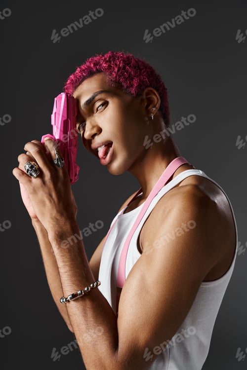 Preview: playful african american man posing in profile sticking out tongue and looking aside with toy gun