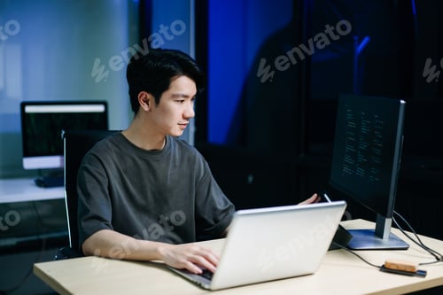 Preview: Young male programmer working with tablet and screen displaying code. Modern tech office setup,