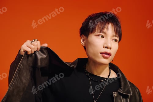 Preview: Stylish young man in a leather jacket poses confidently against a bright orange backdrop