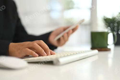 Preview: Close up of businesswoman typing computer keyboard and using smartphone