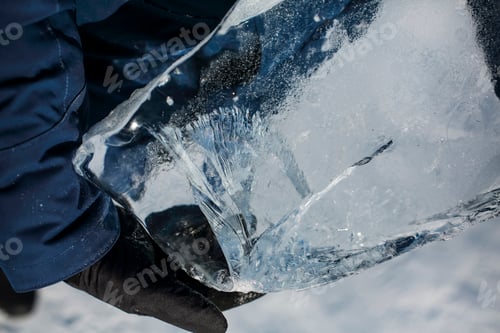 Preview: man wearing winter blue jacket and holding piece of transparent crushed ice cubes in his hands