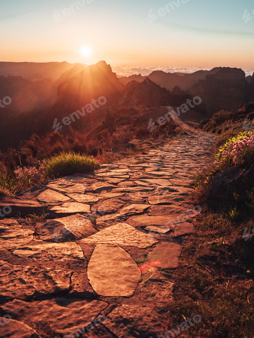 Preview: Narrow stone footpath on the hill with high rough mountains in the background during a warm sunset