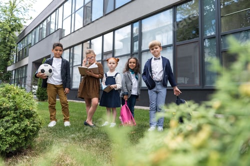 Visualização: grupo de lindas crianças multiétnicas em pé perto da escola e olhando para a câmera