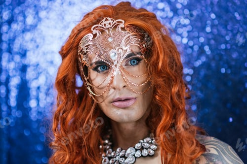 Preview: Drag queen wearing a mask while posing against a glitter background.