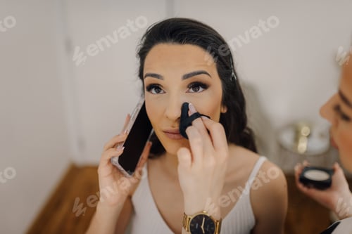 Preview: Makeup artist applying foundation on model's face while talking on phone