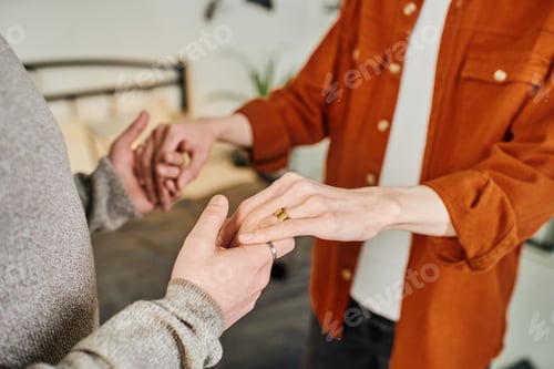 Preview: partial view of gay man holding hands of boyfriend in wedding ring in bedroom
