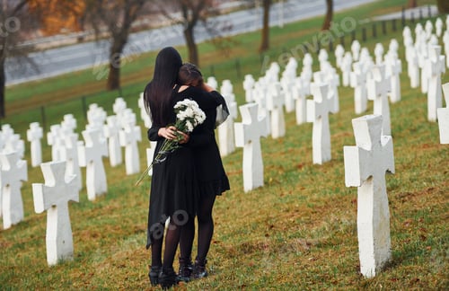 Preview: Two young women in black clothes visiting cemetery with many white crosses