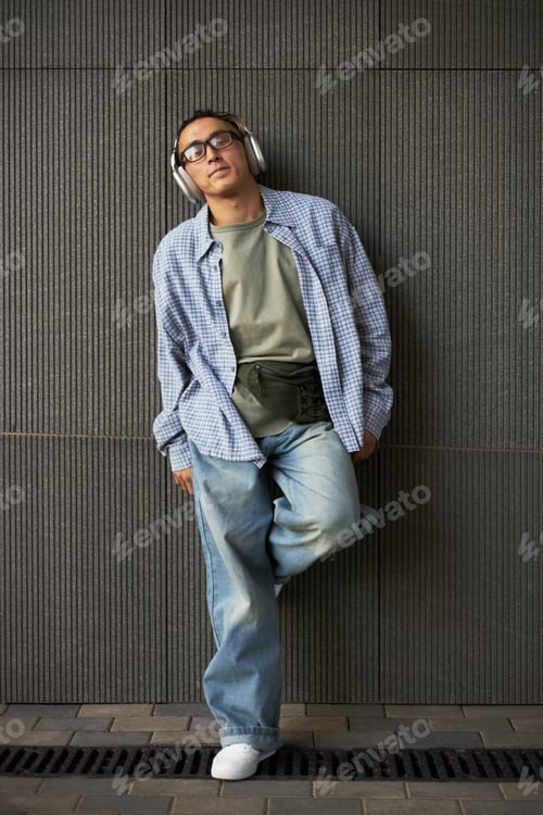 Preview: Young Adult Caucasian Man Listening to Music with Headphones Standing Outdoors